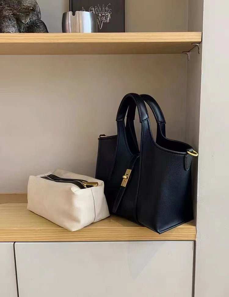 High-end black crossbody handbag with gold zipper, shown with daily accessories for scale reference